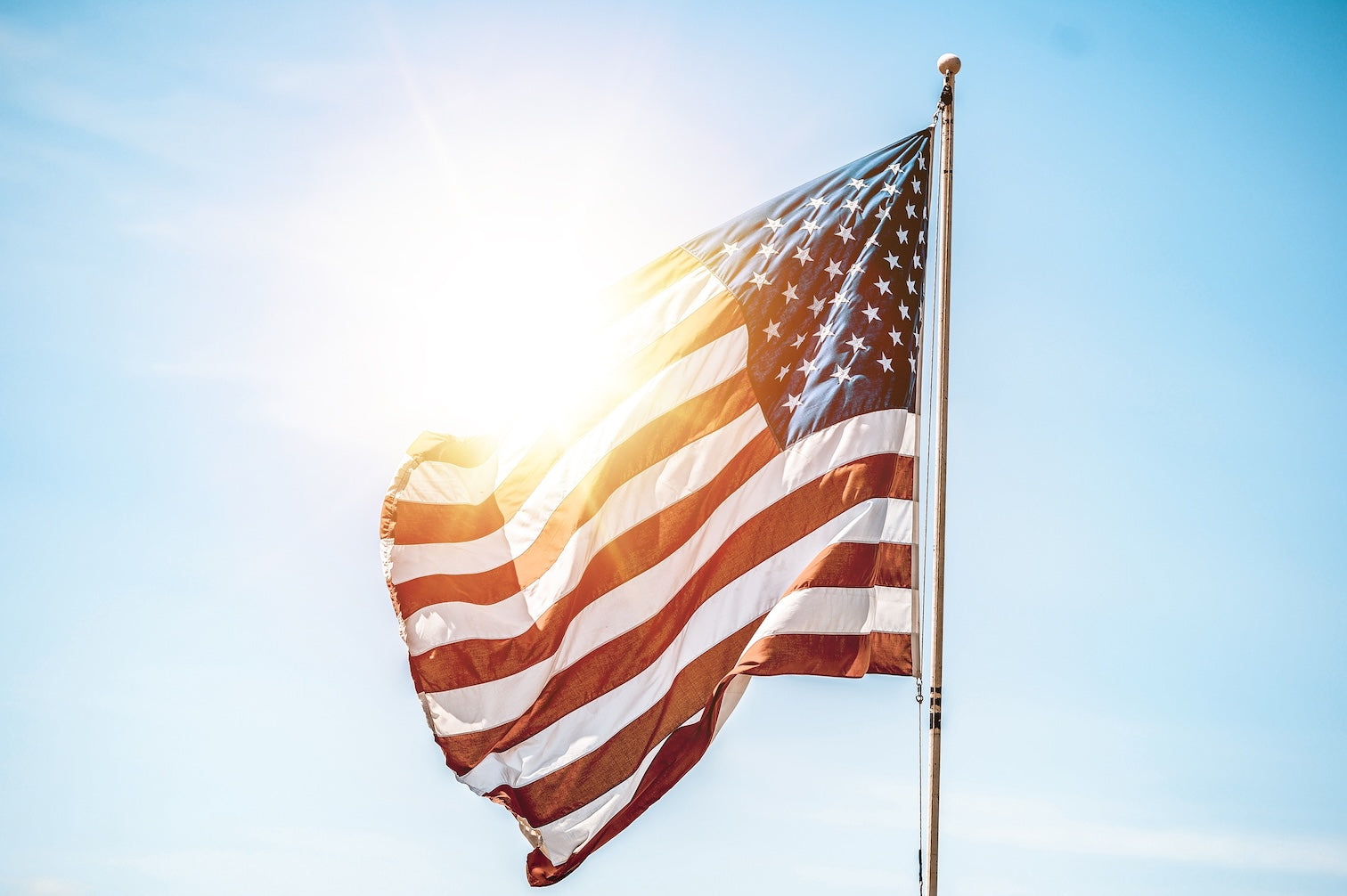 United States flag on a flag pole with the sun shining
