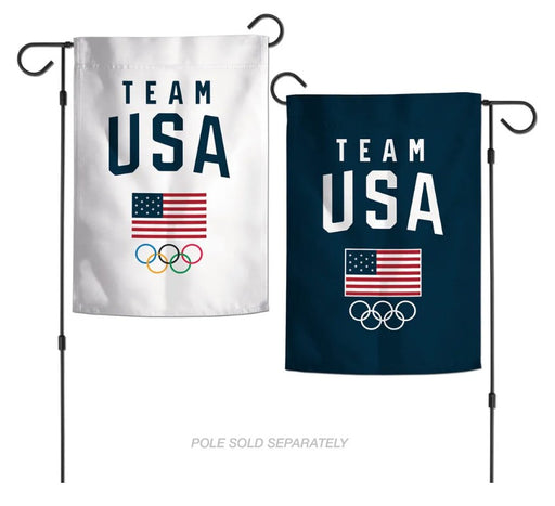 Two vertical garden flags on black metal poles, each printed with 'TEAM USA', an American flag, and the Olympic rings. One flag is white and the other is dark navy blue.